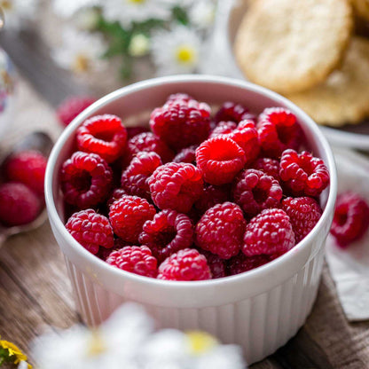 White bowl filled with heritage raspberries on a wooden surface