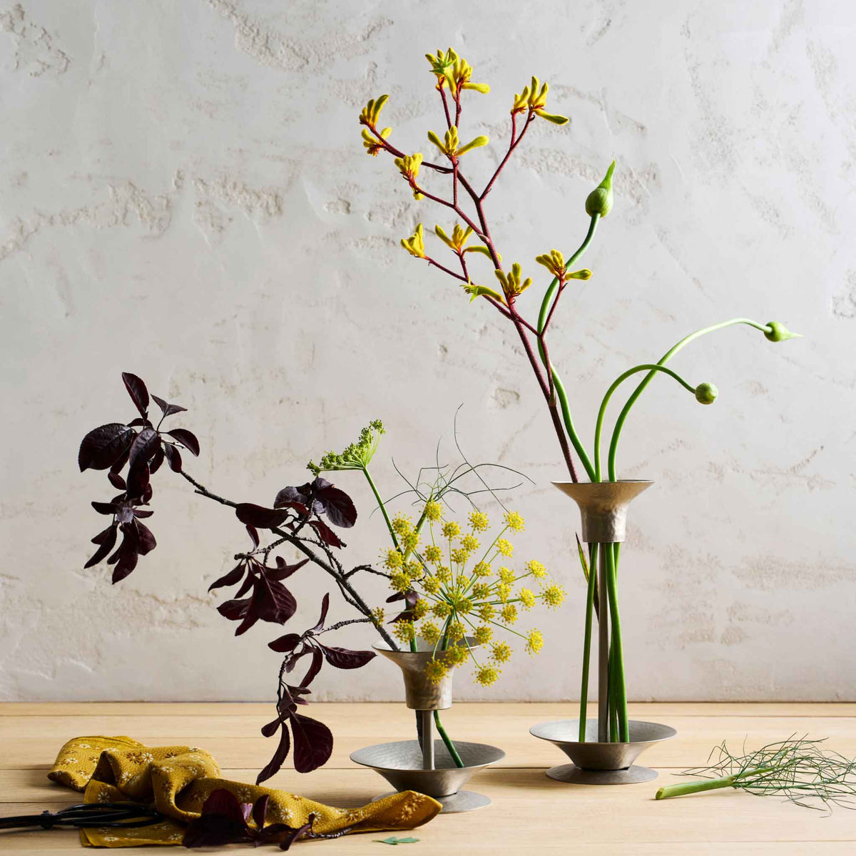 Two arrangements using the collective hammered metal stem vase and bouquet rings on a wooden table and white background